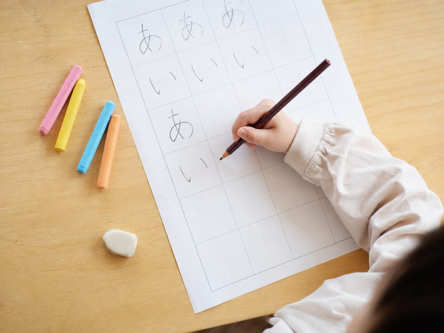 幼児がひらがなの練習シートに鉛筆で「あ」を書いている手元